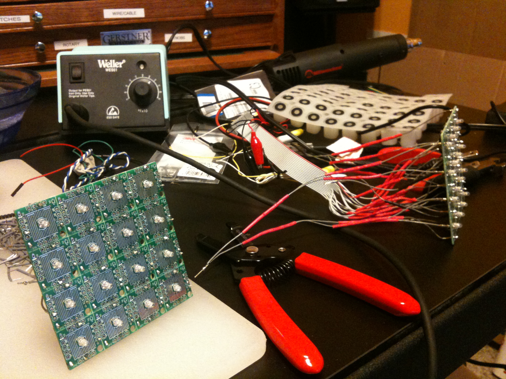 Workbench with a Weller soldering station, a button PCB matrix and a red wiring harness mid-build